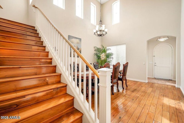 stairs with hardwood / wood-style flooring, plenty of natural light, a chandelier, and a towering ceiling