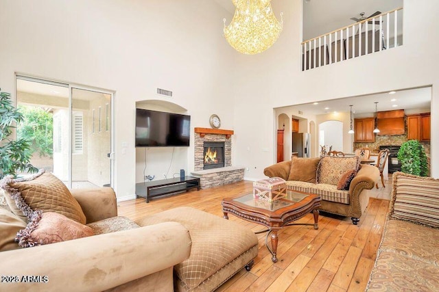 living room with an inviting chandelier, a stone fireplace, and light hardwood / wood-style flooring