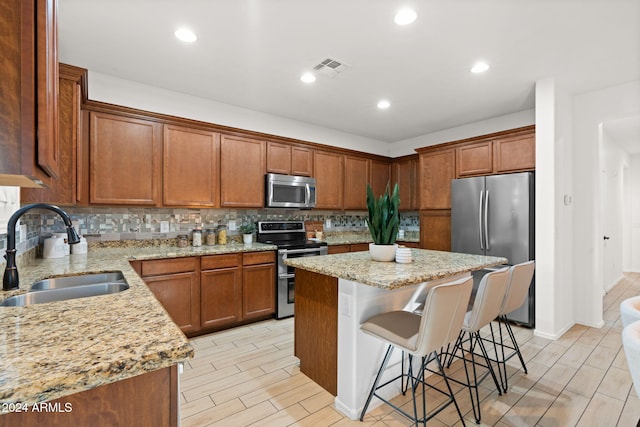 kitchen with light stone counters, stainless steel appliances, sink, a center island, and a breakfast bar area