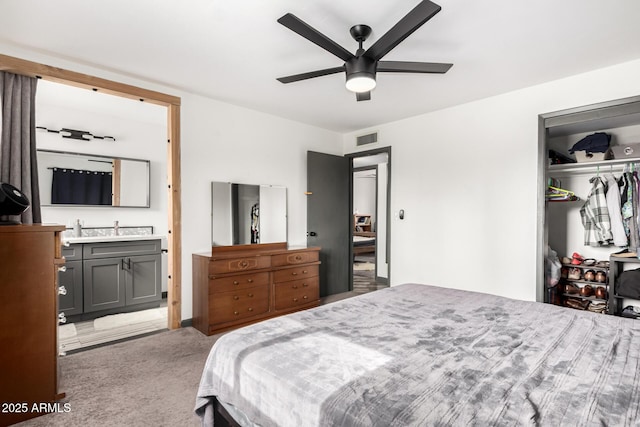 carpeted bedroom with ensuite bathroom, sink, ceiling fan, and a closet