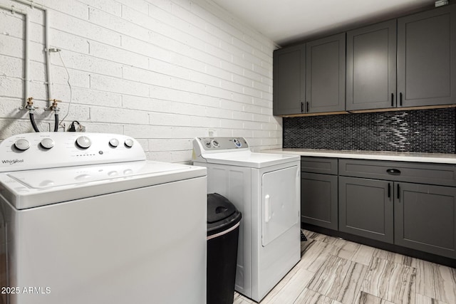 laundry room with cabinets, brick wall, and washer and clothes dryer