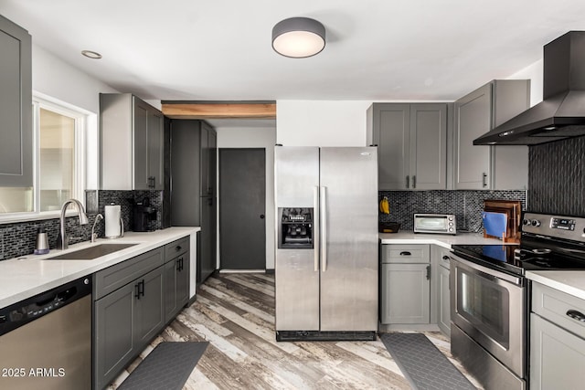 kitchen with wall chimney exhaust hood, appliances with stainless steel finishes, sink, and gray cabinetry