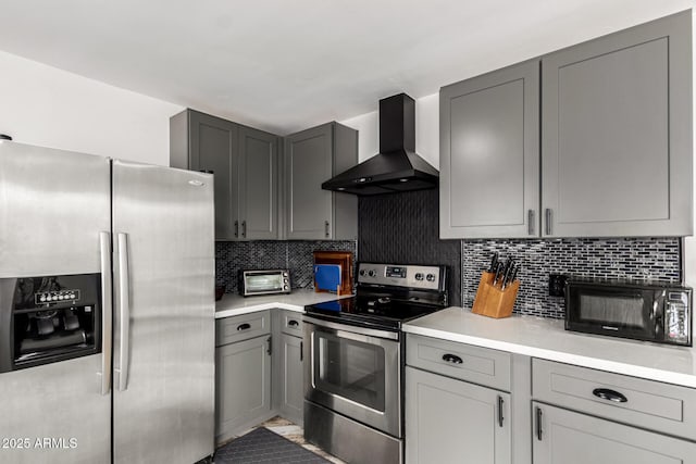 kitchen featuring gray cabinetry, decorative backsplash, stainless steel appliances, and wall chimney exhaust hood