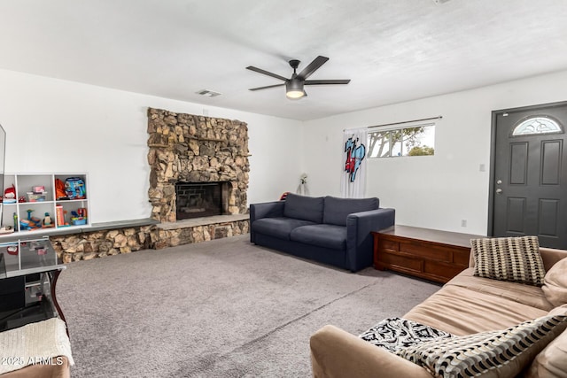 carpeted living room with a stone fireplace and ceiling fan