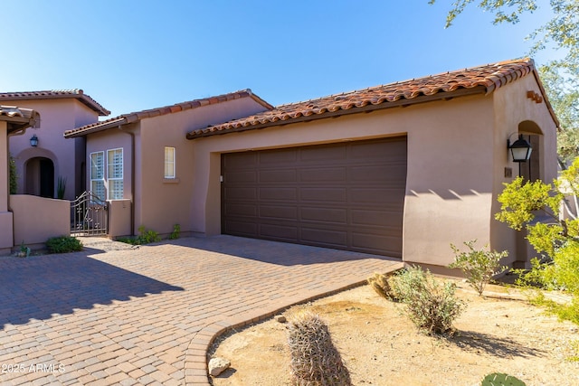 mediterranean / spanish-style home featuring a garage, a gate, decorative driveway, and stucco siding