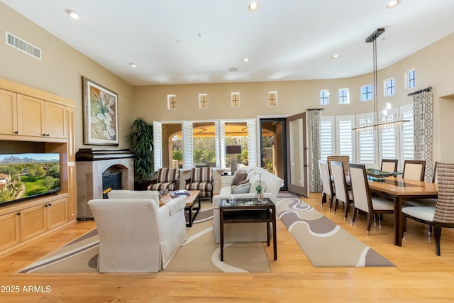 living area with a warm lit fireplace, visible vents, light wood-style floors, and recessed lighting