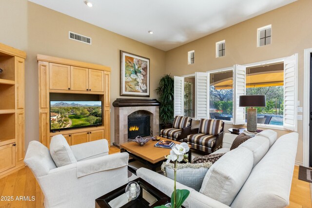 living area featuring a warm lit fireplace, visible vents, light wood finished floors, and recessed lighting