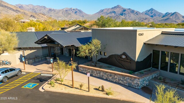 view of front facade with metal roof, a standing seam roof, uncovered parking, a mountain view, and stucco siding