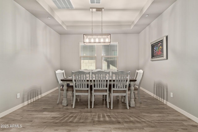 dining area featuring a raised ceiling, wood-type flooring, and an inviting chandelier