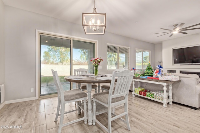 dining space featuring ceiling fan with notable chandelier, a fireplace, and light hardwood / wood-style floors