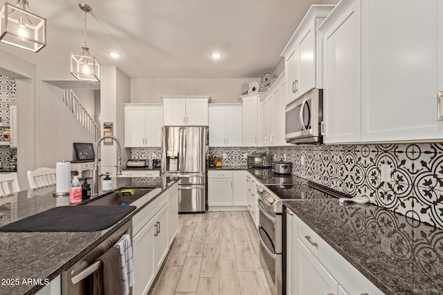 kitchen featuring stainless steel appliances, dark stone counters, white cabinets, and pendant lighting