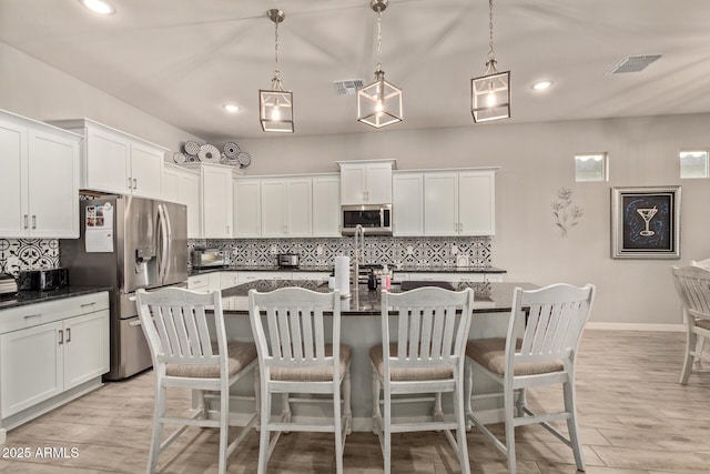 kitchen featuring stainless steel appliances, a center island with sink, and hanging light fixtures