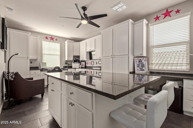 kitchen with ceiling fan, white cabinetry, dark stone countertops, and a kitchen island