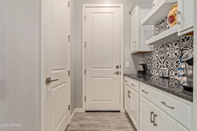 interior space featuring white cabinets, dark stone counters, light hardwood / wood-style floors, and decorative backsplash