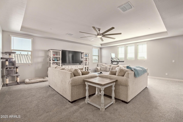 carpeted living room with ceiling fan and a raised ceiling