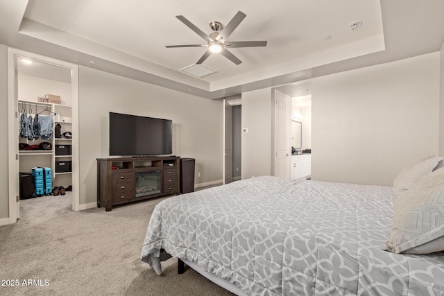 bedroom featuring a spacious closet, a raised ceiling, a closet, light colored carpet, and ceiling fan