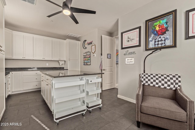 kitchen featuring a kitchen island, white cabinets, ceiling fan, and dark stone counters