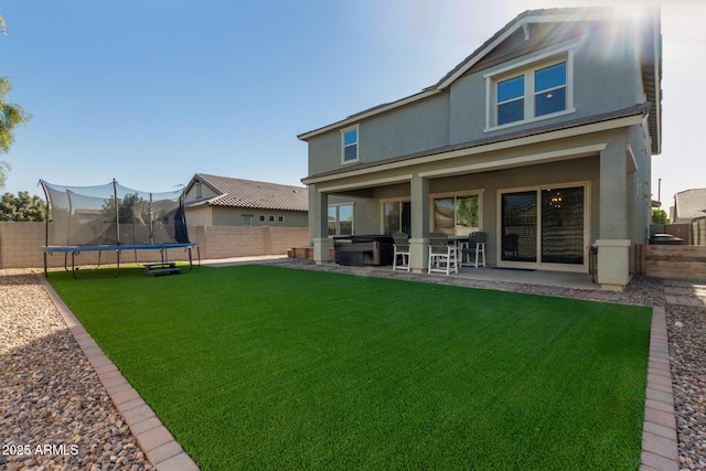 rear view of house featuring a hot tub, a yard, a patio area, and a trampoline