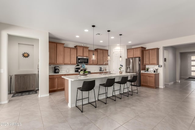 kitchen featuring stainless steel appliances, a sink, brown cabinetry, a kitchen bar, and an island with sink