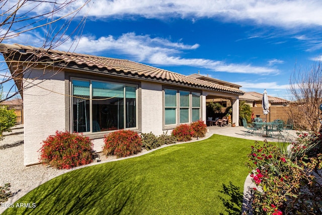 rear view of property featuring a patio, fence, a yard, a tiled roof, and stucco siding