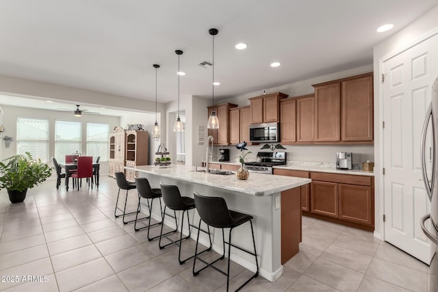 kitchen featuring appliances with stainless steel finishes, brown cabinetry, a sink, and a kitchen breakfast bar