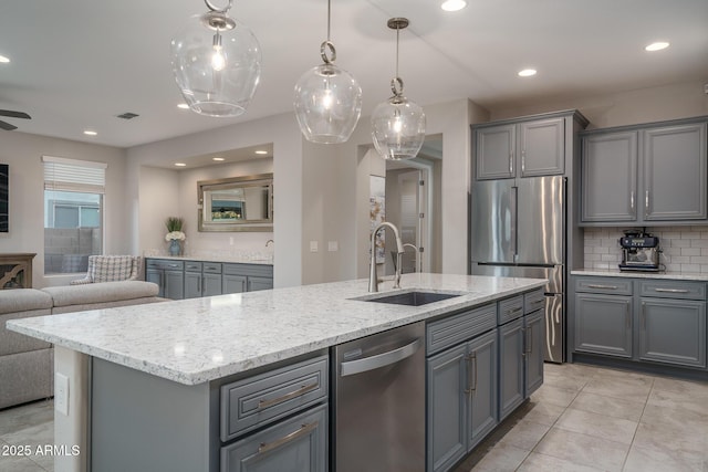 kitchen with stainless steel appliances, an island with sink, gray cabinets, and sink