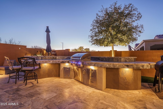 patio terrace at dusk featuring an outdoor kitchen and a grill