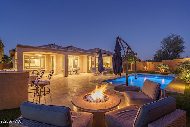 pool at dusk featuring exterior bar, a patio area, and an outdoor fire pit