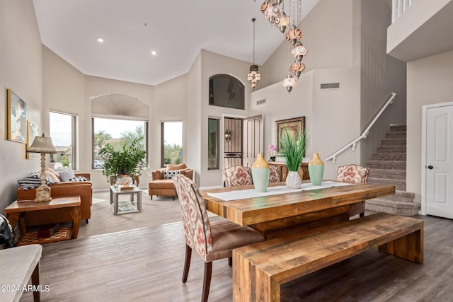 dining space featuring an inviting chandelier, light hardwood / wood-style floors, and a towering ceiling