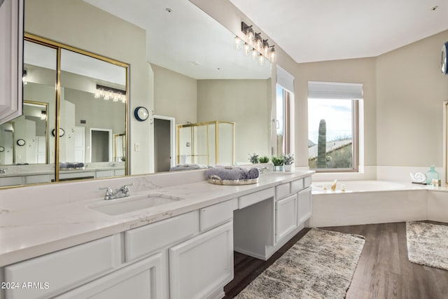 bathroom with double sink, vanity with extensive cabinet space, wood-type flooring, vaulted ceiling, and a tub