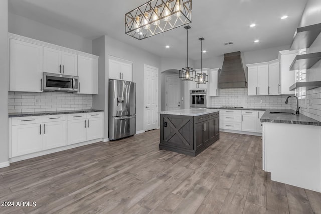 kitchen featuring a kitchen island, white cabinets, premium range hood, hanging light fixtures, and appliances with stainless steel finishes