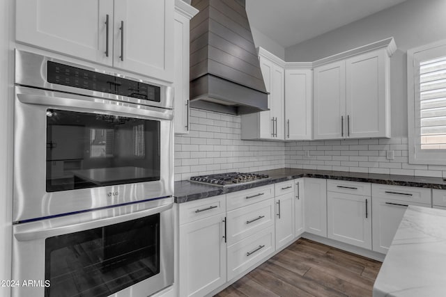 kitchen with dark stone counters, hardwood / wood-style floors, custom range hood, stainless steel appliances, and white cabinets