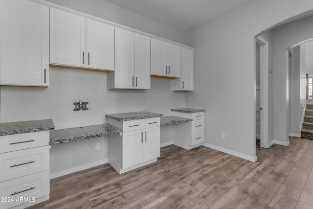 kitchen featuring white cabinets, light hardwood / wood-style flooring, built in desk, and stone countertops