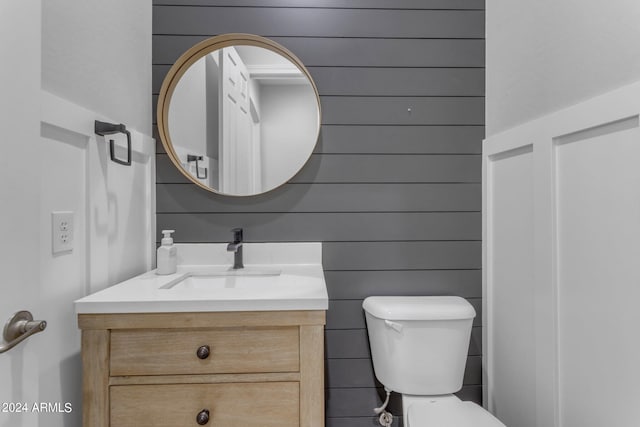 bathroom with vanity, wood walls, and toilet