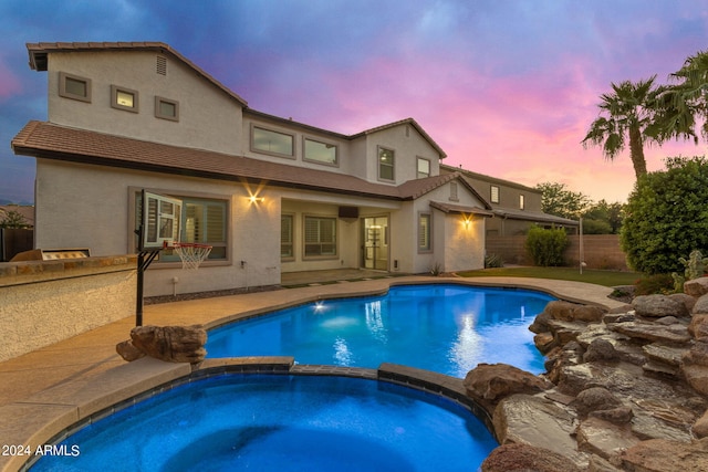 pool at dusk with an in ground hot tub and a patio