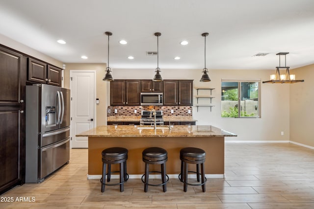 9921 E Acceleration Dr, Mesa, AZ 85212 - kitchen with appliances with stainless steel finishes, a sink, dark brown cabinetry, tasteful backsplash, and a breakfast bar