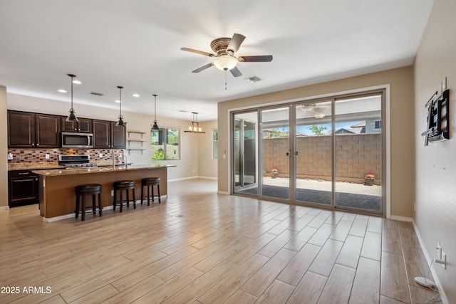 9921 E Acceleration Dr, Mesa, AZ 85212 - kitchen with stainless steel appliances, a breakfast bar area, baseboards, dark brown cabinets, and light wood-style flooring