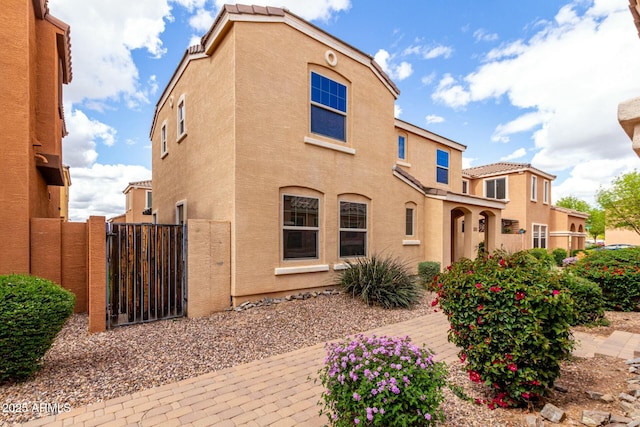 back of property with a tile roof, a gate, and stucco siding