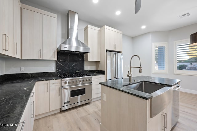 kitchen with dark stone countertops, a center island with sink, high end appliances, and wall chimney range hood