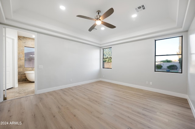 empty room with ceiling fan, light hardwood / wood-style flooring, plenty of natural light, and a tray ceiling