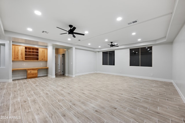 unfurnished living room featuring ceiling fan, light wood-type flooring, and built in desk