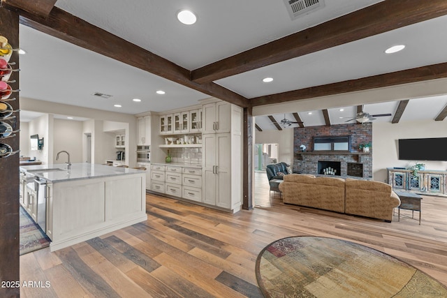 kitchen with visible vents, a sink, stainless steel oven, a brick fireplace, and light wood-type flooring