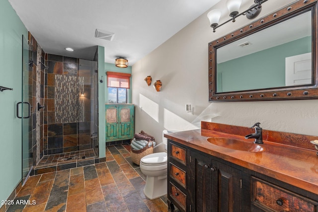 bathroom with visible vents, toilet, stone finish flooring, a shower stall, and vanity