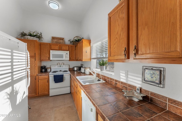 kitchen with brown cabinetry, white appliances, tile counters, and a sink