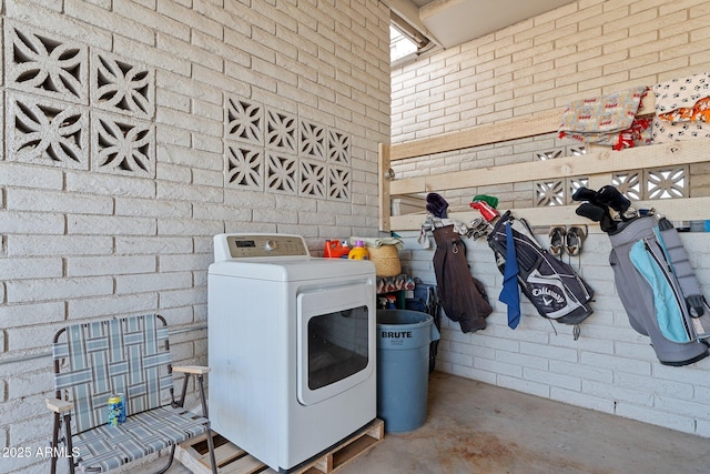 clothes washing area featuring washer / dryer, brick wall, and laundry area