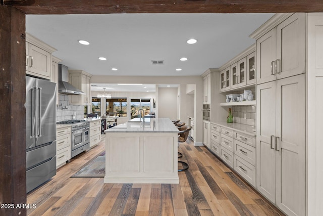 kitchen featuring wall chimney range hood, high quality appliances, visible vents, and light wood finished floors