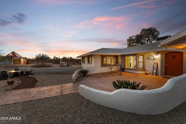 back of house at dusk with a patio area and stucco siding