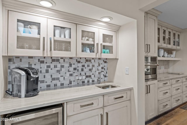 kitchen with glass insert cabinets, wine cooler, stainless steel oven, light stone counters, and a sink