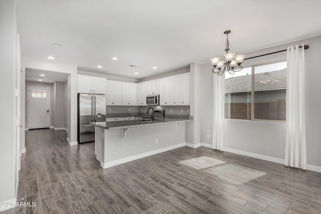 kitchen featuring appliances with stainless steel finishes, a sink, white cabinets, a peninsula, and wood finished floors