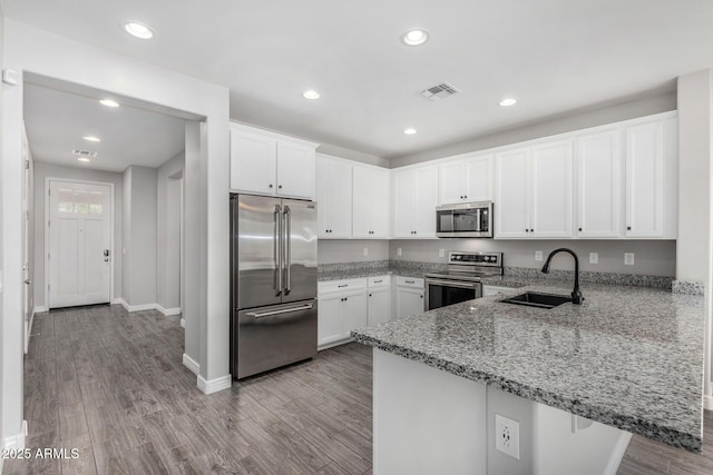 kitchen featuring appliances with stainless steel finishes, a sink, a peninsula, white cabinetry, and light stone counters